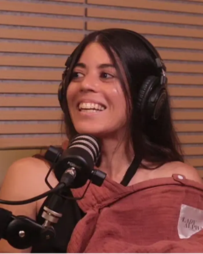 Dagmi sonriendo con audífonos frente al micrófono del podcast